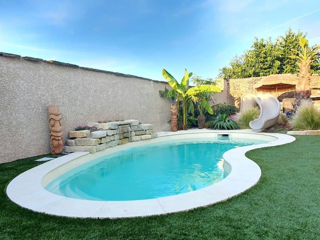Piscine coque Alizé de chez Piscines Ibiza avec végétation et toboggan